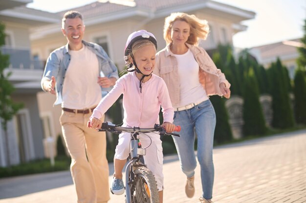 A cute blonde girl learning to ride a bike with her parents