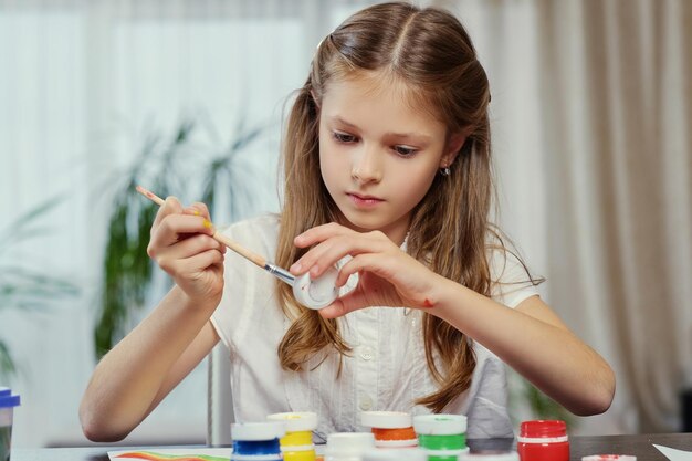 Cute blonde girl painting with acrylic paint in art studio class.