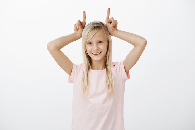 Cute blonde girl showing devil horns and smiling
