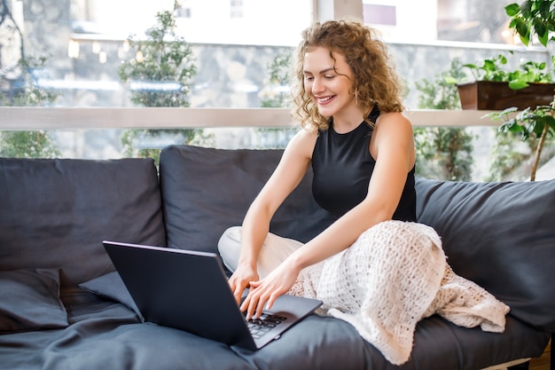 Cute blonde girl spend time at home on weekend, working with laptop and smiling