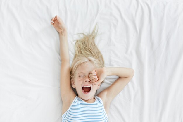 Cute blonde little girl stretching in white bed