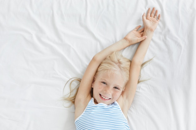 Free photo cute blonde little girl stretching in white bed