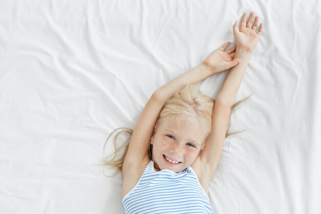 Cute blonde little girl stretching in white bed