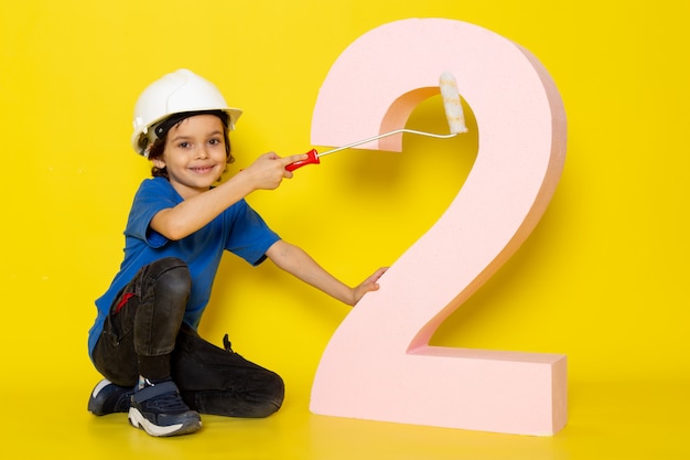 Cute boy adorable sweet in blue t-shirt and dark trousers near number figure on yellow wall