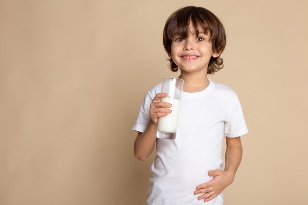 милый мальчик, обожаемый в белой футболке, пьющий белое цельное молоко на розовом столе