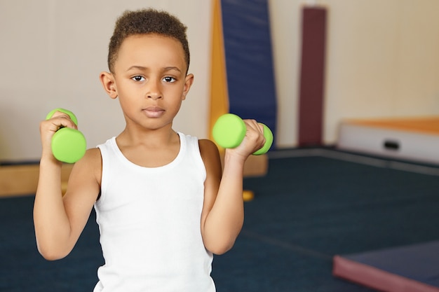 Cute boy athlete of African appearance doing physical exercises at gym after school