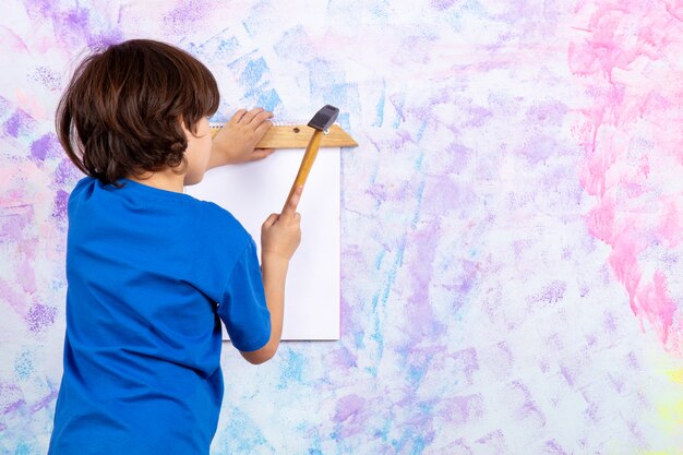 cute boy back view in blue t-shirt working with hammer on colorful wall