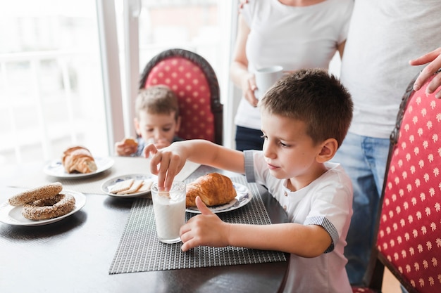 Cute boy dipping biscuit in glass of milk during breakfast