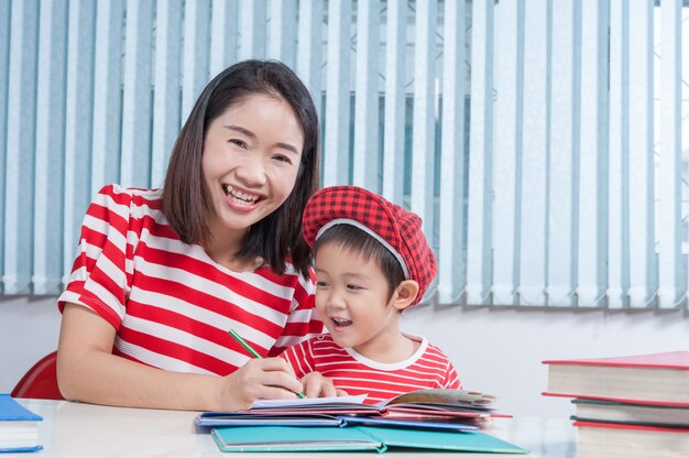 かわいい男の子、彼の学校の宿題を母親と一緒に家で、彼は本に書いている