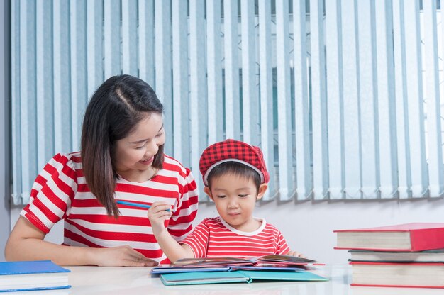 かわいい男の子、彼の学校の宿題を母親と一緒に家で、彼は本に書いている