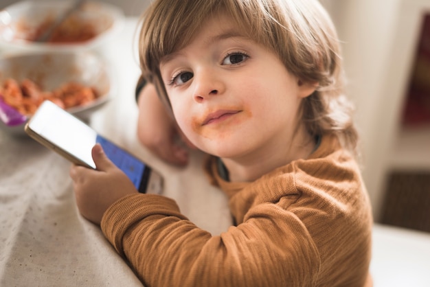 テーブルで携帯電話を保持しているかわいい男の子