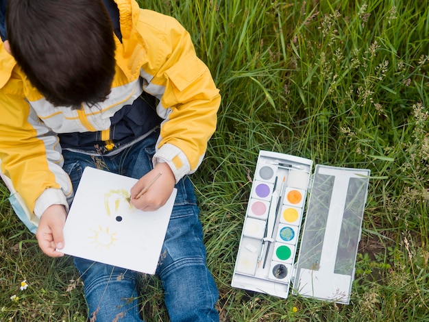 Free photo cute boy in raincoat painting top view