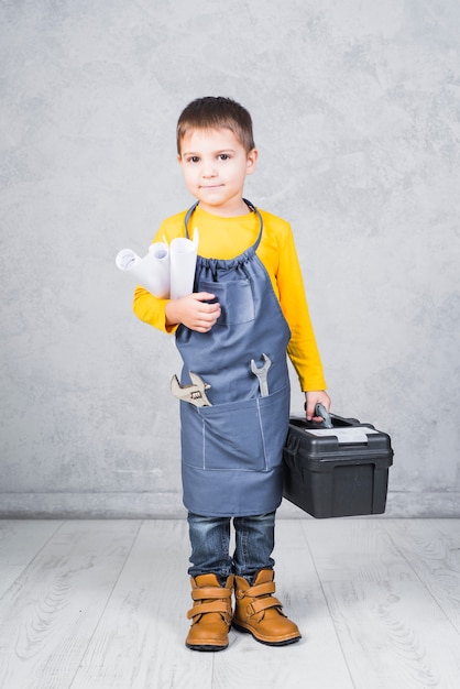 Бесплатное фото Милый мальчик стоит с ящиком для инструментов и бумажными рулонами