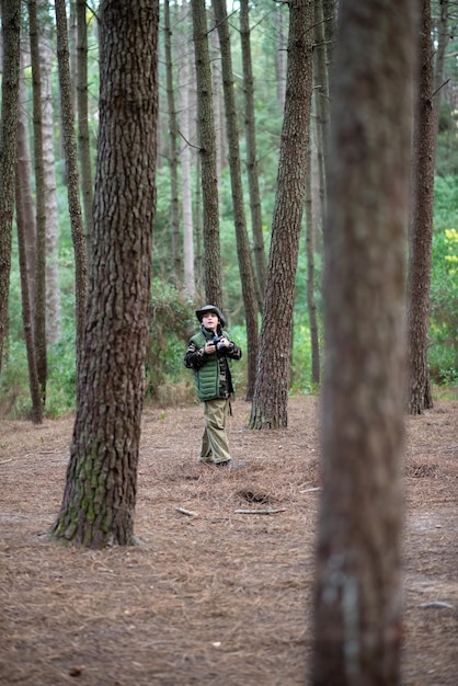 Free photo cute boy with camera in forest. schoolboy in coat and panama taking pictures, walking. childhood, nature, leisure concept