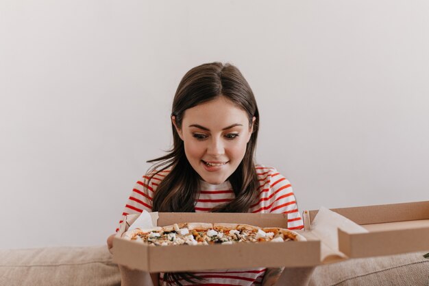 Cute brunette bites her lip while looking at delicious pizza