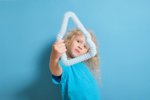 Симпатичная кавказская девушка с вьющимися светлыми волосами играет с игрушкой pop it tube на синем фоне, трендовая игрушка для развития мелкой моторики рук, антистрессовая трескающая трубка