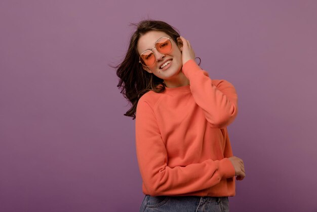 Cute caucasian young brunette girl in glasses and blouse looks at camera on purple background Leisure lifestyle and beauty concept