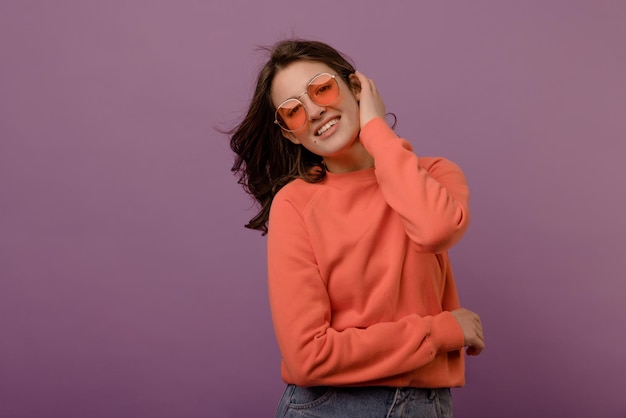 Cute caucasian young brunette girl in glasses and blouse looks at camera on purple background Leisure lifestyle and beauty concept