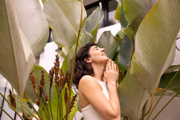 Cute caucasian young brunette woman with closed eyes in summer top stands among palm leaves Concept of rest and recovery