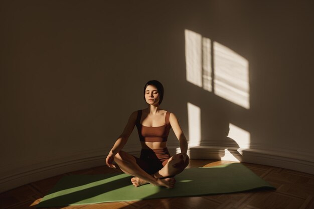Cute caucasian young woman doing breathing exercises during yoga class at home Focused brunette with closed eyes wears top and leggings Leisure relaxation and lifestyle concept