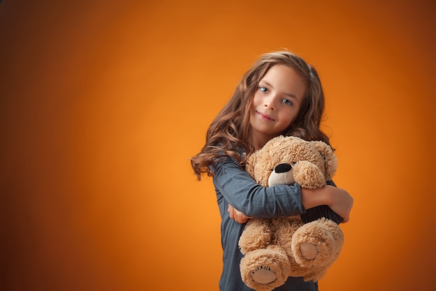 The cute cheerful little girl on orange background