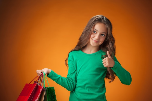 The cute cheerful little girl with shopping bags on orange background