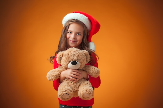 The cute cheerful little girl with Teddy bear on orange background