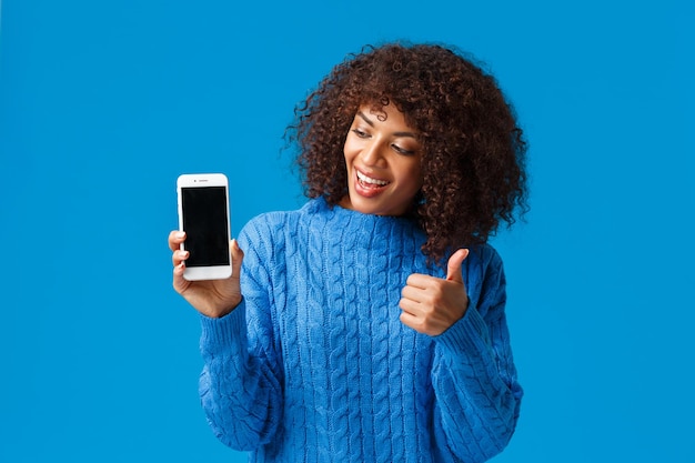 Cute and cheerful satisfied africanamerican woman showing something on display make thumbup gesture ...