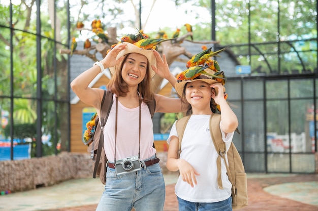 Free photo cute child feeling happy and smiles with her mother while playing with parrot bird.