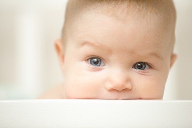 Cute child sucking a wooden board of the white cot