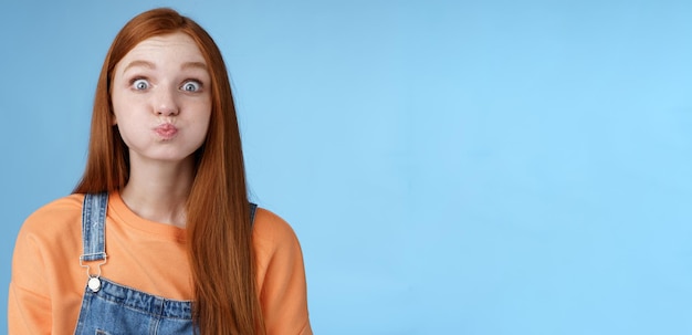 Free photo cute childish playful charming redhead girl popping blue eyes staring camera hold breath inhale air