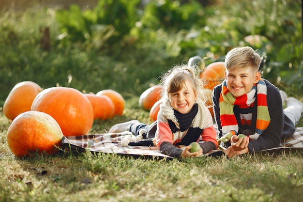 Cute childresn sitting on a garden near many pumpkins