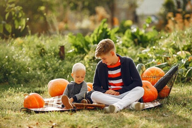 Cute childresn sitting on a garden near many pumpkins