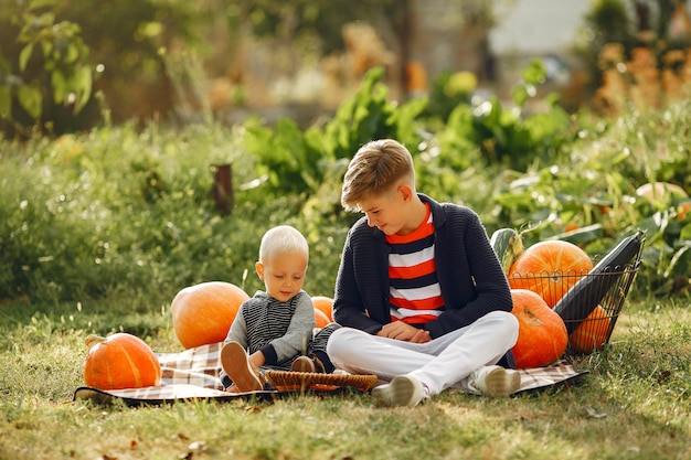 Cute childresn sitting on a garden near many pumpkins