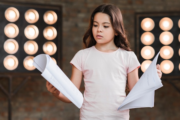 Cute confused girl holding scripts in hands