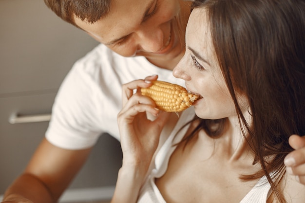 Free photo cute couple in a kitchen. lady in a white t-shirt. pair at home eat boiled corn.