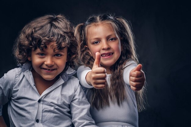 Cute couple of a little boy with curly hair and beautiful girl have fun at a studio. Isolated on the dark textured background.