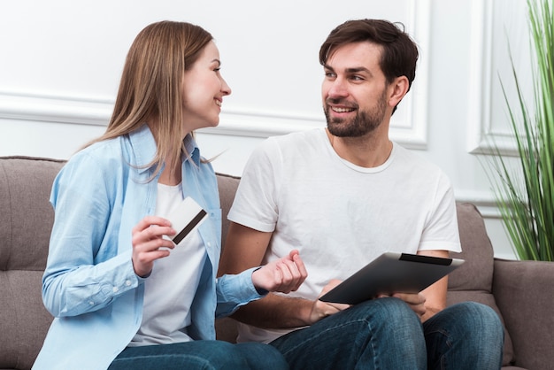 Cute couple looking at each other and holding digital devices for online purchases