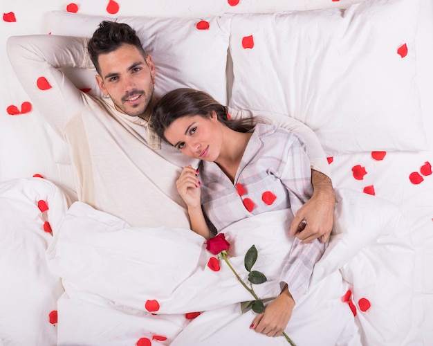 Cute couple lying in bed with rose petals 