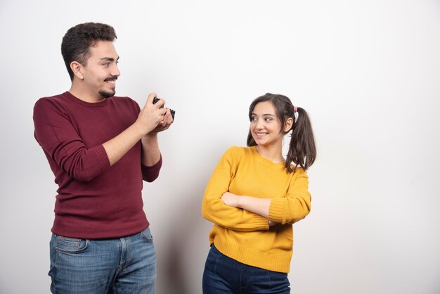 Cute couple taking pictures with camera and posing over a white wall.