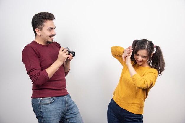 Cute couple taking pictures with camera and posing over a white wall.