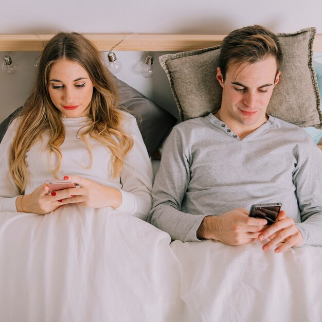 Cute couple using smartphones in bed