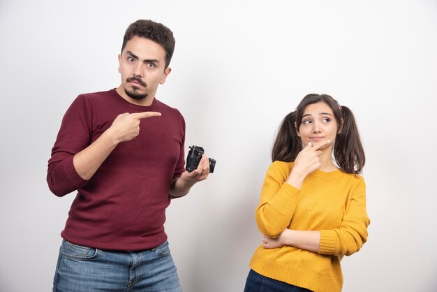 Cute couple with camera posing over a white wall.