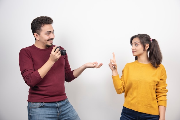 Cute couple with camera posing over a white wall.