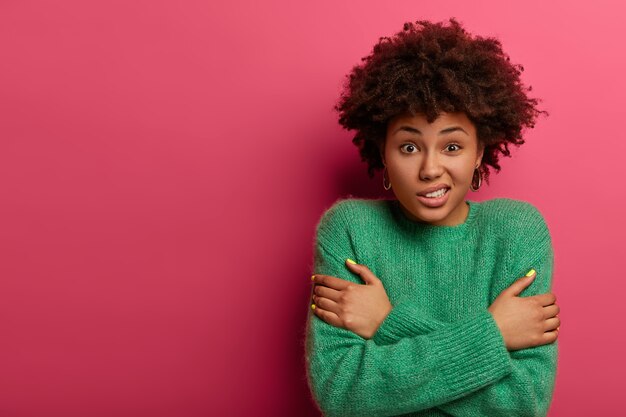 cute curly woman crosses arms over body, trembles during freezing cold winter weather