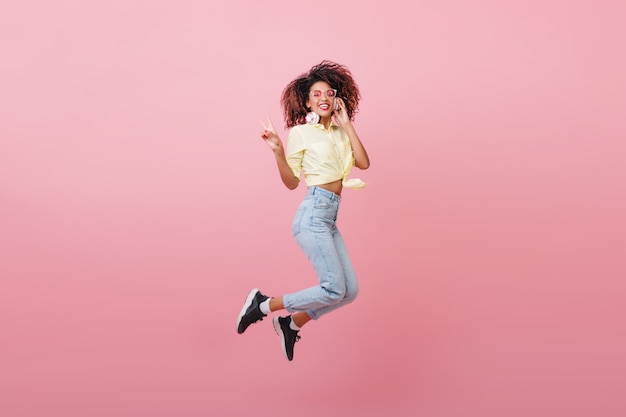 Free photo cute curly woman in yellow shirt expressing happy emotions with smile. magnificent african hipster girl jumping.