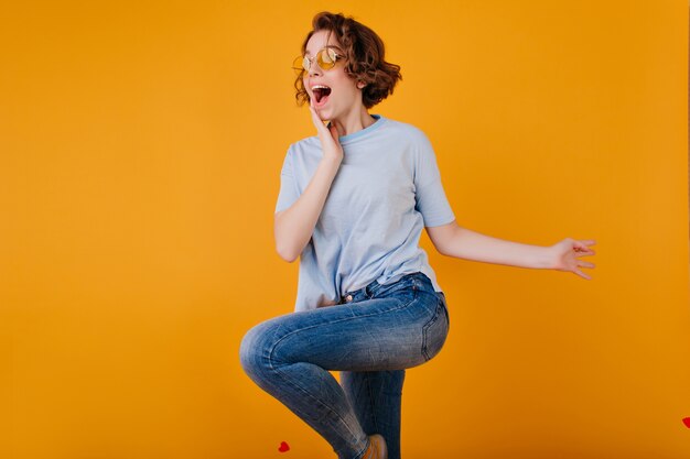 Cute dark-haired lady with excited face expression dancing in jeans