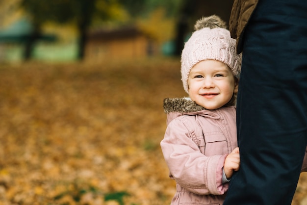 Cute daughter holding on father leg in autumn park
