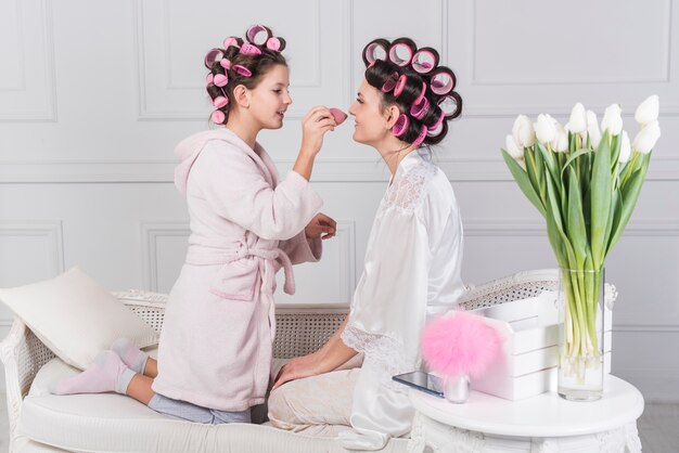 Cute daughter putting powder on mothers face