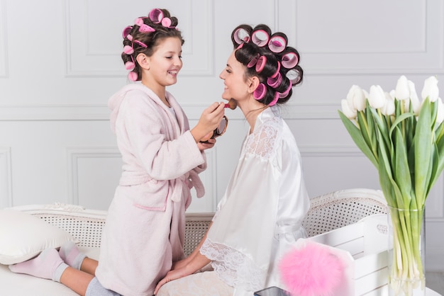 Cute daughter putting powder on mothers neck